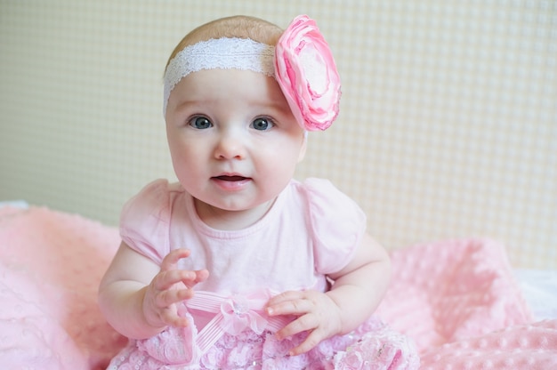 Kleines Mädchen in einem rosa Kleid sitzt auf dem Bett.