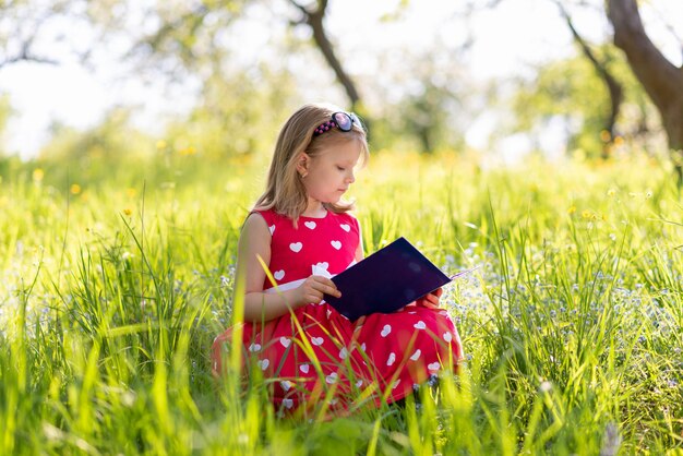 Kleines Mädchen in einem roten Kleid liest ein Buch