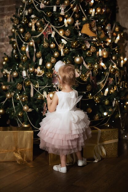 Kleines Mädchen in einem schönen Kleid schmückt den Weihnachtsbaum