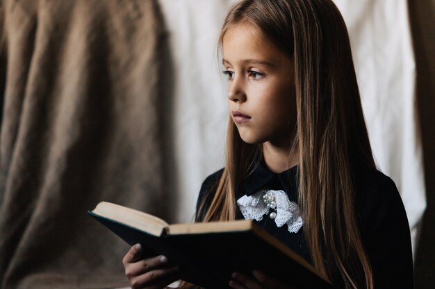 Kleines Mädchen in einem schwarzen Kleid hält ein grünes Buch und liest es.