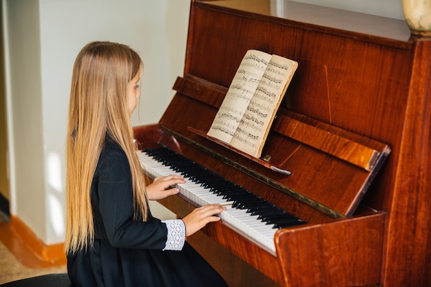 Kleines Mädchen in einem schwarzen Kleid lernt, Klavier zu spielen. Das Kind spielt ein Musikinstrument.