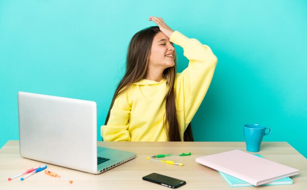 Kleines Mädchen in einem Tisch mit einem Laptop über isoliertem blauem Hintergrund hat etwas erkannt und beabsichtigt die Lösung