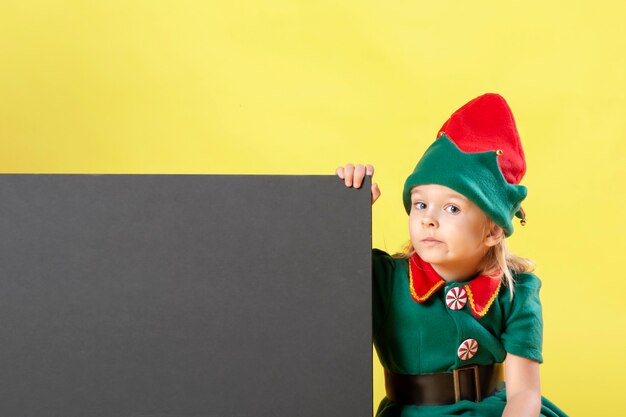 Foto kleines mädchen in einem weihnachtselfenkostüm mit einem nachdenklichen gesicht.