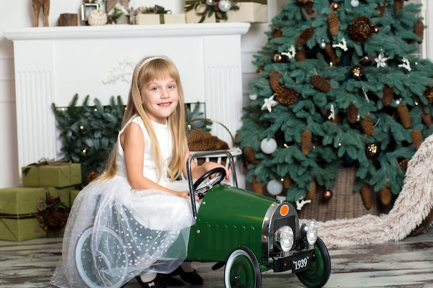 Kleines mädchen in einem weißen kleid fährt ein auto der weinlesekinder in den weihnachtsdekorationen