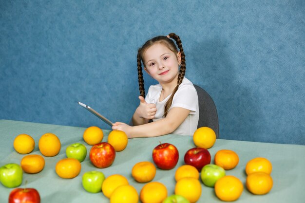 Kleines Mädchen in einem weißen T-Shirt hält eine Tablette in den Händen und studiert die Früchte