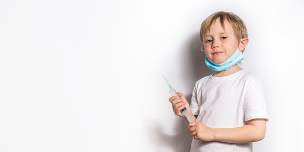 Kleines Mädchen in einem weißen T-Shirt und einer medizinischen Maske, die Arzt spielt, der eine Spritze hält