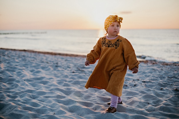 Kleines Mädchen in orientalischer Kleidung, das bei Sonnenuntergang am Strand entlang geht