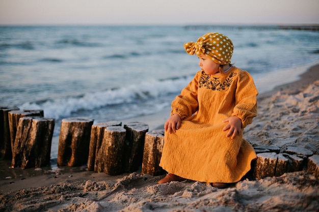 Kleines Mädchen in orientalischer Kleidung sitzt auf Wellenbrecher am Ostseestrand