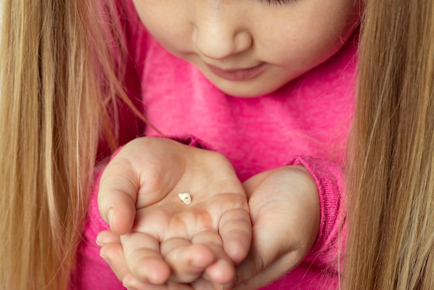 Foto kleines mädchen in rosa hält einen gefallenen milchzahn in ihren handflächen. zahnhygienekonzept.