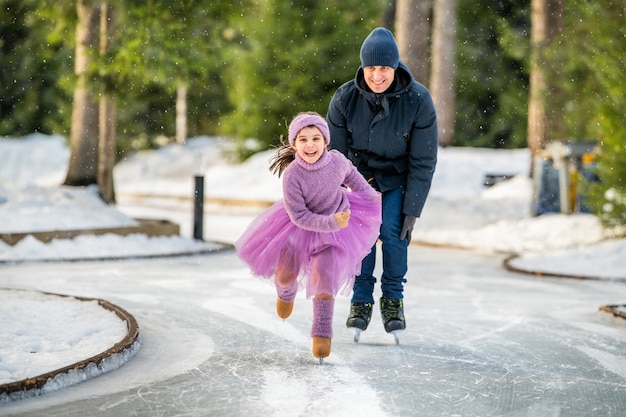 Kleines Mädchen in rosa Pullover und vollem Rock reitet am sonnigen Wintertag auf einer Eisbahn im Freien im Park