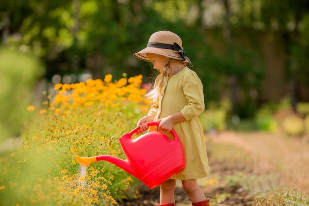 kleines Mädchen in rotem Gummi bootswatering Blumen im Garten