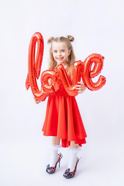 Kleines Mädchen in rotem Schlafanzug großer Ballon farik mit der Aufschrift Liebe auf dunkelbraunem Holzhintergrund mit roten Herzen das Konzept des Valentinstags