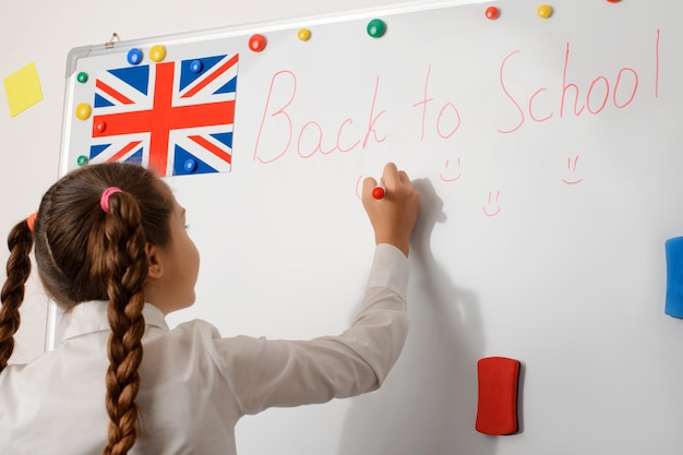 Kleines Mädchen in Schuluniform, das auf Englisch auf einer Tafel schreibt