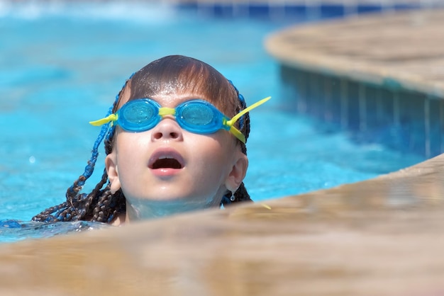 Kleines Mädchen in Schutzbrillen, das im blauen Poolwasser im Freien schwimmen lernt Sommererholungsaktivitätskonzept