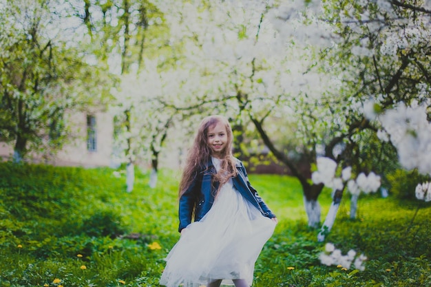 Kleines Mädchen in schwarzer Jacke und weißem Kleid tanzt im Frühlingskirschgarten