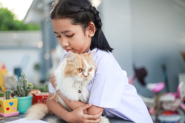 Kleines Mädchen in thailändischer Studentenuniform umarmt ihre Perserkatze