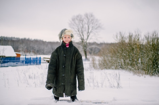 Kleines Mädchen in übergroßer Jacke, die im Winter auf Schnee steht