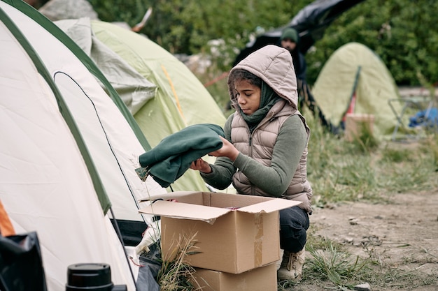 Kleines Mädchen in warmer Jacke, die Box mit neuer Kleidung auspackt