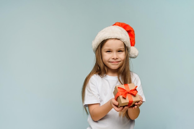 Kleines Mädchen in Weihnachtsmütze und mit Weihnachtsgeschenk auf blauem Hintergrund Platz kopieren Weihnachten und ein frohes neues Jahr Konzept