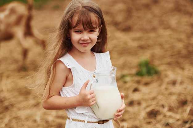 Kleines Mädchen in weißer Kleidung ist im Sommer im Freien mit Milch auf dem Bauernhof