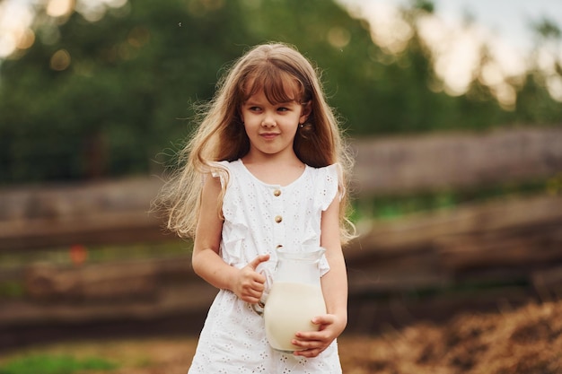 Kleines Mädchen in weißer Kleidung ist im Sommer im Freien mit Milch auf dem Bauernhof