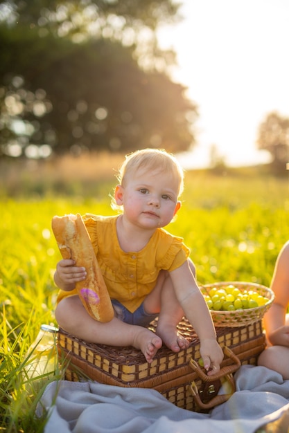 Kleines Mädchen isst frisches Baguette und Obst bei einem Picknick bei Sonnenuntergang in der Natur