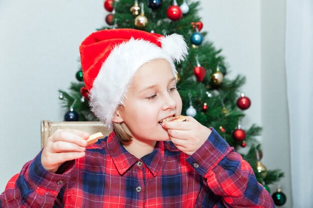 Kleines Mädchen isst Kekse vor dem Hintergrund des Weihnachtsbaums