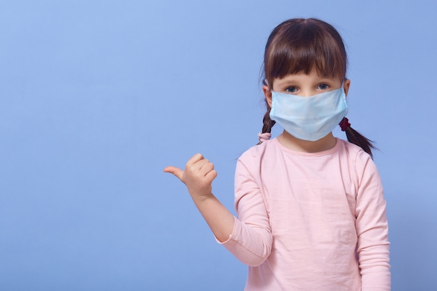 Kleines Mädchen kleidet medizinische Schutzmaske und Rosenhemd, posierend