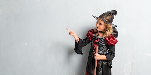 Kleines Mädchen kleidete als Hexe für Halloween-Feiertage an und zeigte auf das Seitliche