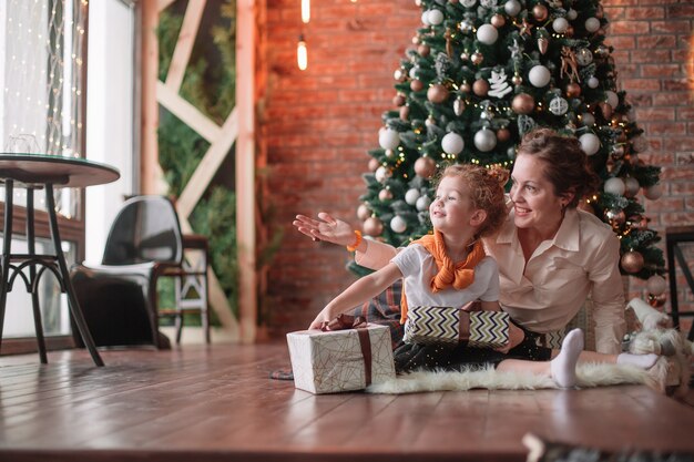 Kleines Mädchen küsst ihre Mutter in der Nähe des Weihnachtsbaumes