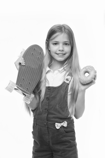 Kleines Mädchen Lächeln mit Skateboard und Donut, isoliert auf weiss Kinder-Skater mit Donut und Longboard Skateboard-Kind mit Junk-Food Sport und Energie Ernährung für Snacks und Desserts Diät-Konzept