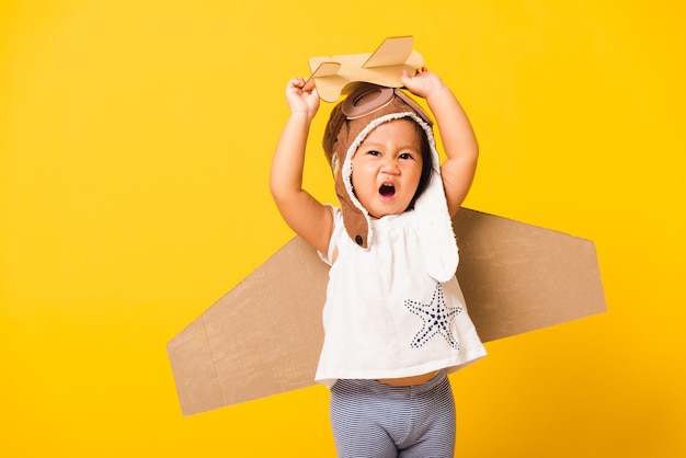 Kleines Mädchen lächeln tragen Pilotenhut spielen und Schutzbrillen mit Spielzeugkarton Flugzeugflügel fliegen