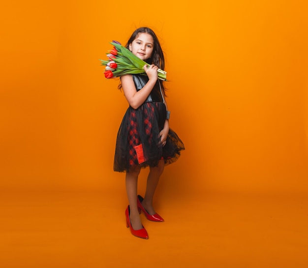 Kleines Mädchen lächelt in einem Kleid und großen roten Schuhen hält einen Blumenstrauß auf gelbem Hintergrund Platz für Text