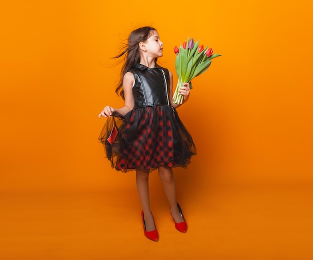 Kleines Mädchen lächelt in einem Kleid und großen roten Schuhen hält einen Blumenstrauß auf gelbem Hintergrund Platz für Text