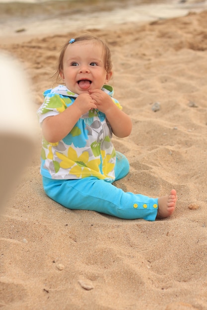 Kleines Mädchen lächelt und sitzt blaues Gelb des Sandklage,