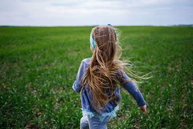 Kleines Mädchen läuft auf grünem Gras auf dem Feld, sonniges Frühlingswetter, Lächeln und Freude des Kindes, blauer Himmel mit Wolken