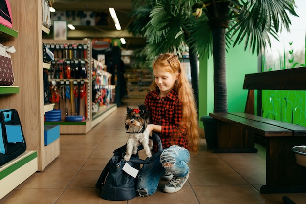 Kleines Mädchen legt ihren Welpen in Tasche, Zoohandlung. Kinderkaufausrüstung in der Zoohandlung, Zubehör für Haustiere