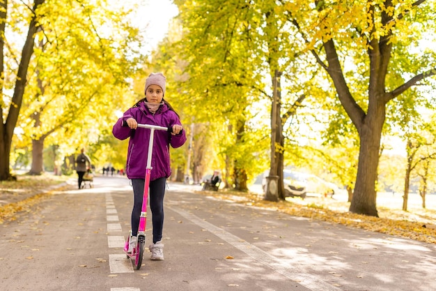 Kleines Mädchen lernt im Herbst in einem Park einen Roller zu fahren