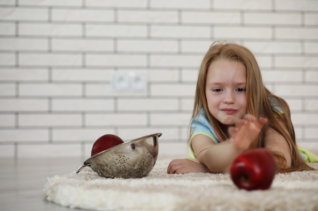 Kleines Mädchen liegt auf dem Boden und isst einen Apfel
