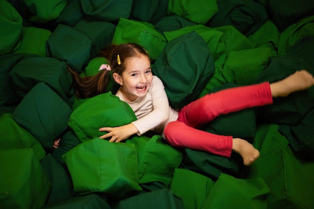 Kleines Mädchen liegt auf grünen, weichen Würfeln im Spielplatzpark Kind in aktiven Unterhaltungen