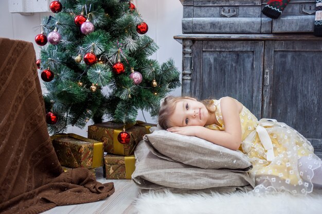 Kleines Mädchen liegt auf Kissen in einem gelben Kleid, Weihnachten.