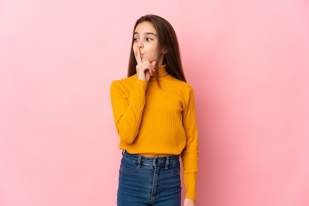 Kleines Mädchen lokalisiert auf rosa Wand, die ein Zeichen der Stille Geste zeigt Finger in den Mund setzen