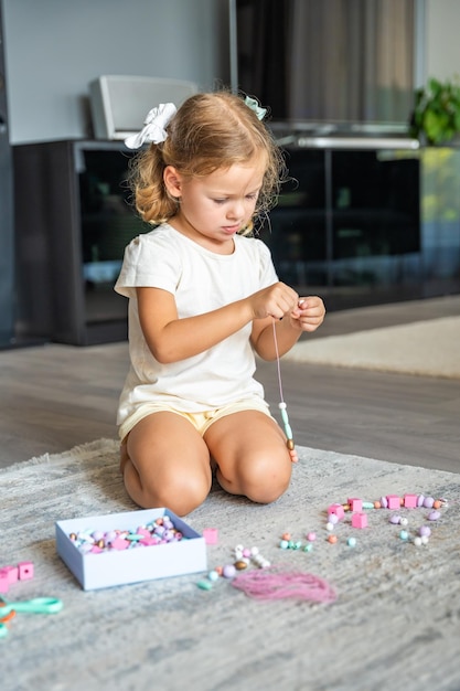 Foto kleines mädchen macht ein holzperlenarmband zu hause wohnzimmer kinderkreativität und die entwicklung der feinen motorik