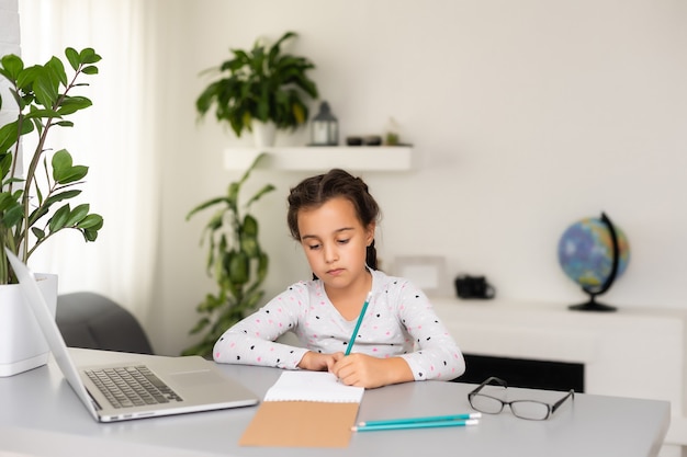 Kleines Mädchen macht ihre Hausaufgaben zu Hause und benutzt einen Laptop