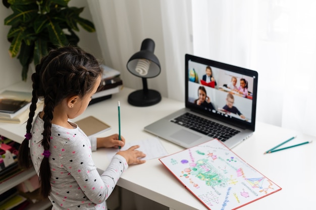 Kleines Mädchen macht ihre Hausaufgaben zu Hause und benutzt einen Laptop