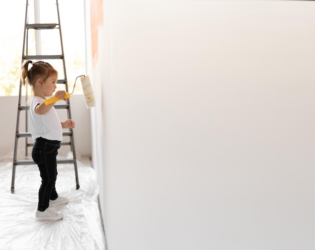 Kleines Mädchen malt die Wand mit einer Rolle. Konzept zur Renovierung des Hauses.