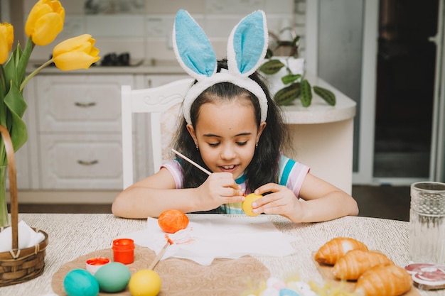 Kleines Mädchen malt Ostereier Glückliche Familie bereitet sich auf Ostern vor Niedliches kleines Mädchen mit Hasenohren am Ostertag