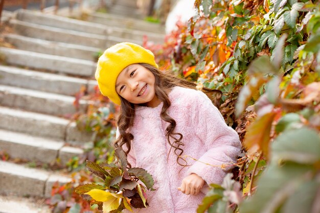 Kleines Mädchen mit asiatischen Aussehenshüten im Herbst schöne Blätter, die einen Blumenstrauß halten