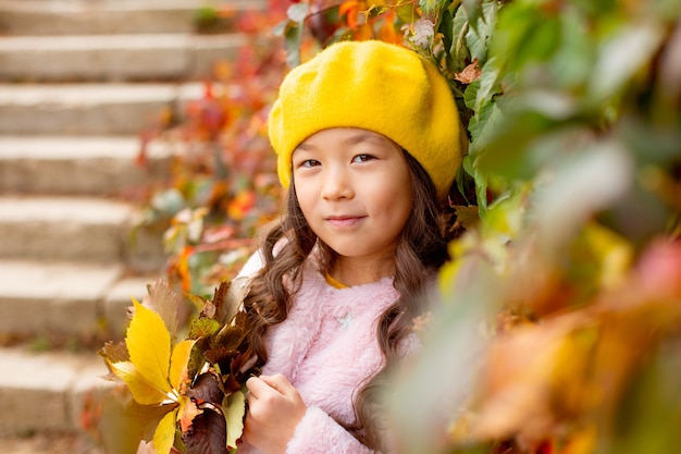 Kleines Mädchen mit asiatischen Aussehenshüten im Herbst schöne Blätter, die einen Blumenstrauß halten