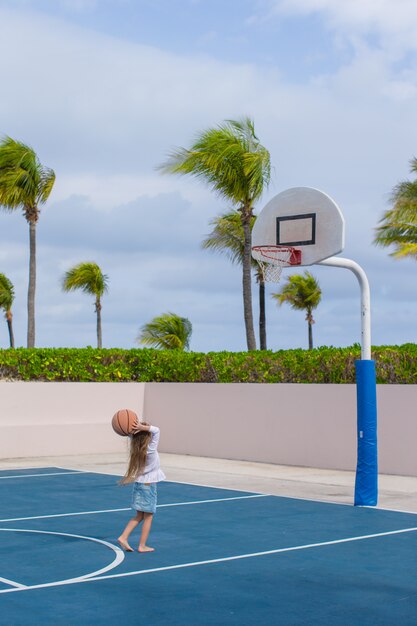 Kleines Mädchen mit Basketball auf Gericht am tropischen Erholungsort